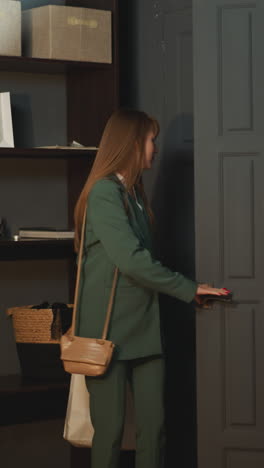 young female worker in business suit comes home carrying paper bags with food. tired woman enters apartment in evening after hard working day