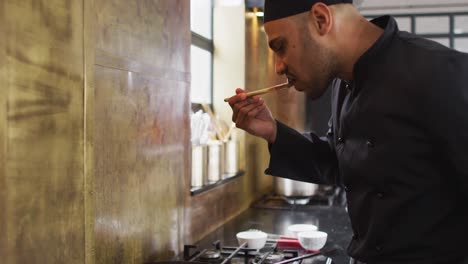 Mixed-race-male-chef-preparing-a-dish-and-smiling-in-a-kitchen-