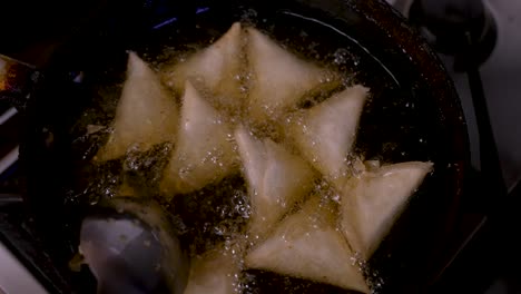 overhead view of samosas being stirred in hot bubbling oil in frying pan