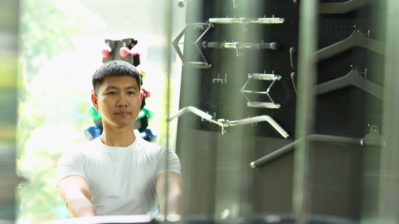 運動好きの男性が、モダンで明るいジムでシーテッドケーブルローに取り組んでいます。