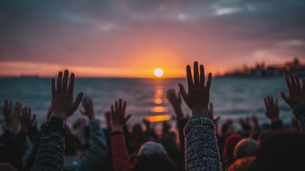 A Serene Gathering by the Shore: Silhouetted Hands Reach Upward in Celebration as the Sun Sets Over the Tranquil Waters, Illuminating a Moment of Unity and Hope
