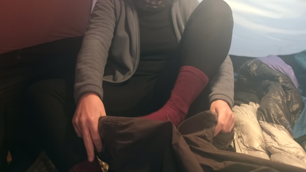 una chica en una tienda se pone pantalones de membrana antes de escalar