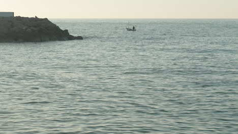 fishing boat floats towards horizon, surrounded by vast expanse of sea water