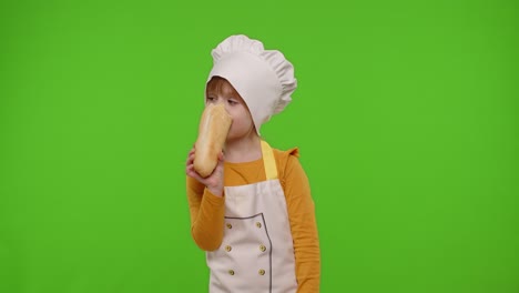 child girl kid dressed in apron and hat like chef cook eating fresh tasty baguette, fooling around