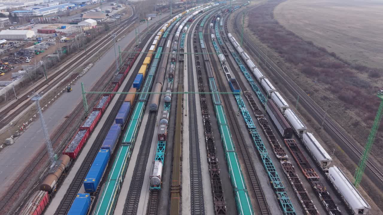 Luftaufnahme eines großen Rangierbahnhofs, gefüllt mit Güterzügen und Frachtwaggons auf parallelen Gleisen. Das Video repräsentiert modernen Schienenverkehr, Logistikabläufe und die Verteilung von Fracht