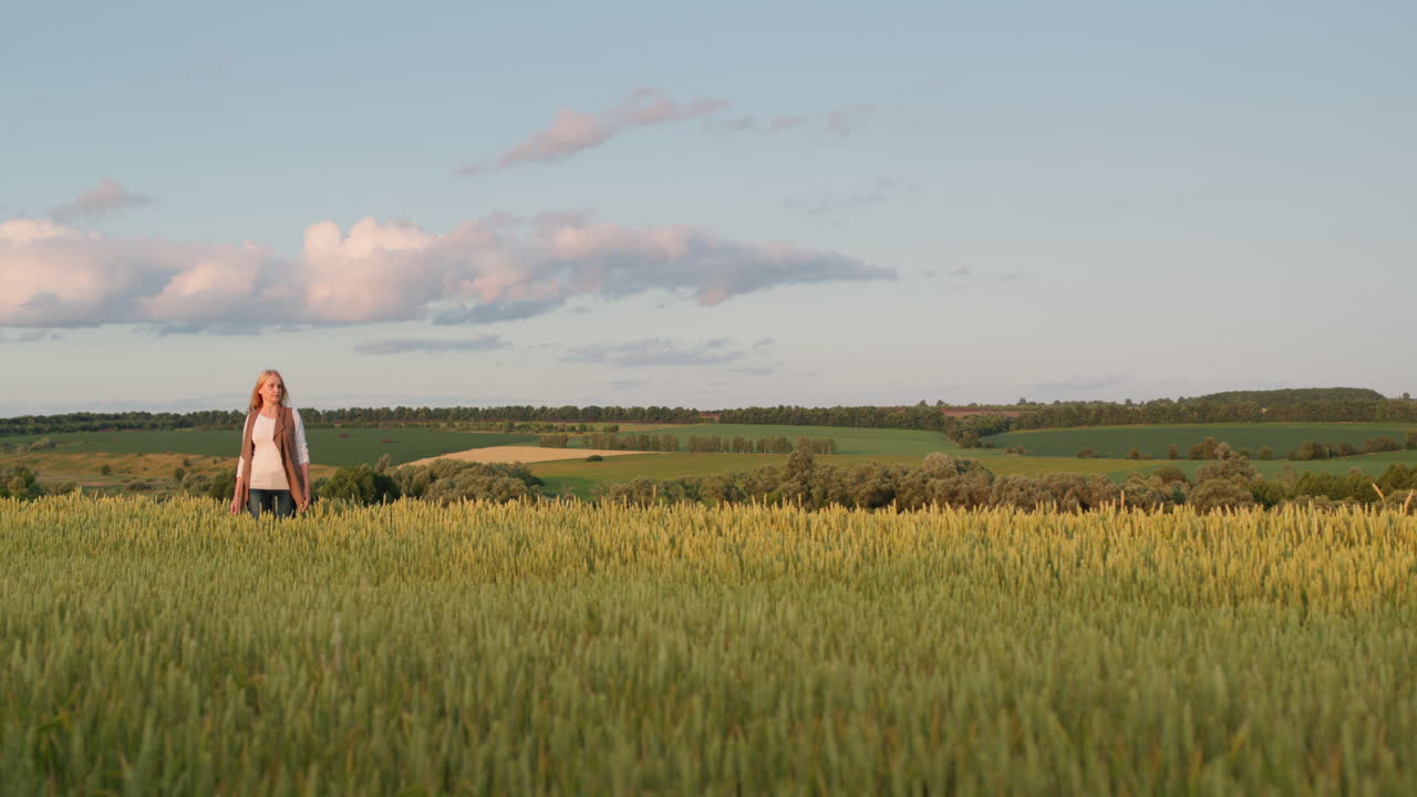 una mujer está de pie frente a un pintoresco paisaje rural con un campo de trigo y un bosque en la distancia. paisaje pastoral