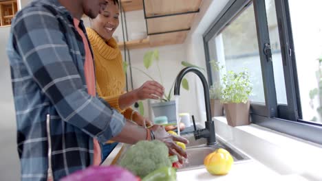 feliz pareja afroamericana enjuagando verduras en la cocina, cámara lenta