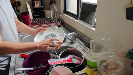 Man-washes-the-dishes-while-he-watches-videos-on-a-tablet