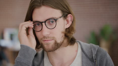 close up portrait of cute young man geek puts on glasses student geek looking at camera slow motion