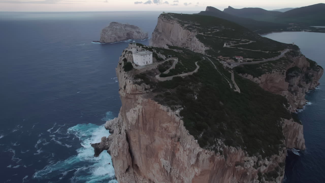 cabo caccia, cerdeña: vista aérea en órbita sobre el faro y viendo las olas que se rompen en la base de la roca