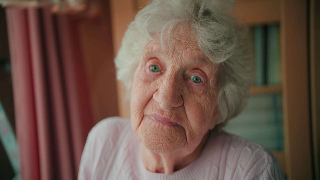 Close-up face of a sad old woman with deep wrinkles winking her eyes