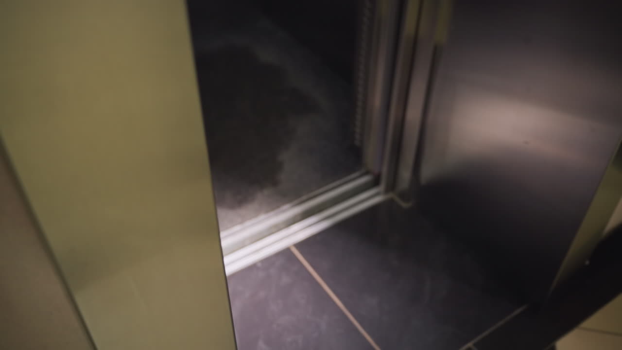 Interior of elevator with shiny metal walls, close-up of floor with tiles, waiting for passengers, elevator not in motion, modern building design, corporate office space, quiet and empty