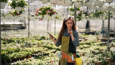 red-haired woman gardener with tablet walking in a greenhouse with plants