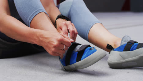 low section of caucasian woman putting on climbing shoes at indoor climbing wall