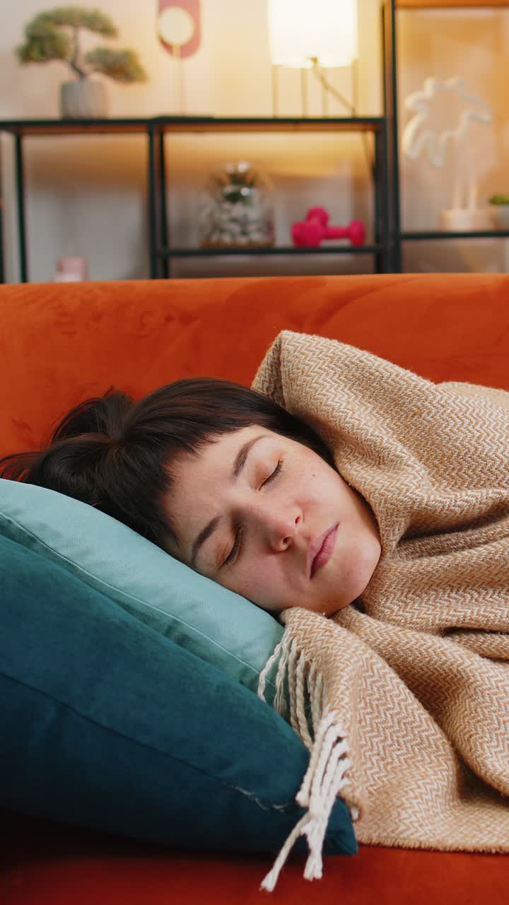 Donna caucasica stanca che dorme tranquillamente, coperta con una coperta sul divano, riposando pacificamente con un sonno salutare