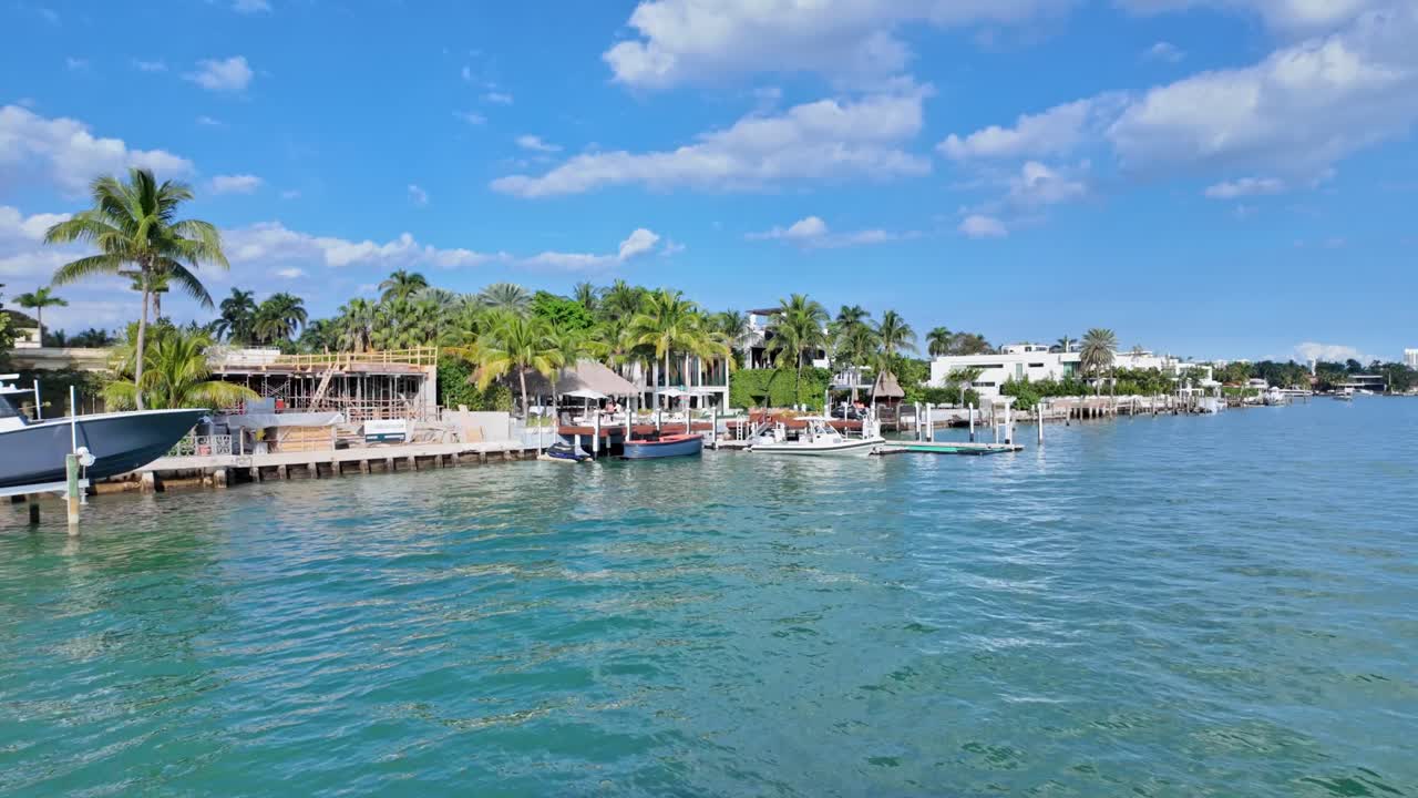 Aerial flight over river showing luxury villa and private yacht pier in Miami during sunny day, Florida