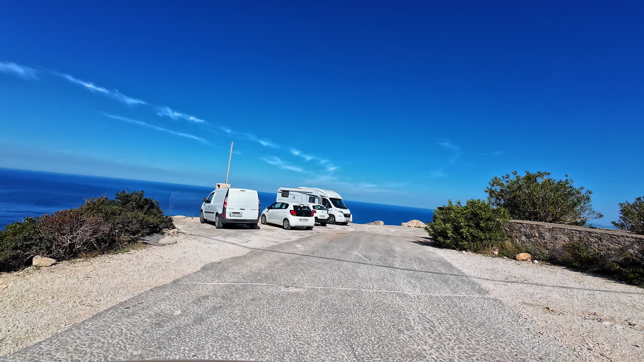 Camper Vans and Cars Parked on a Scenic Cliffside Road Overlooking the Blue Sea