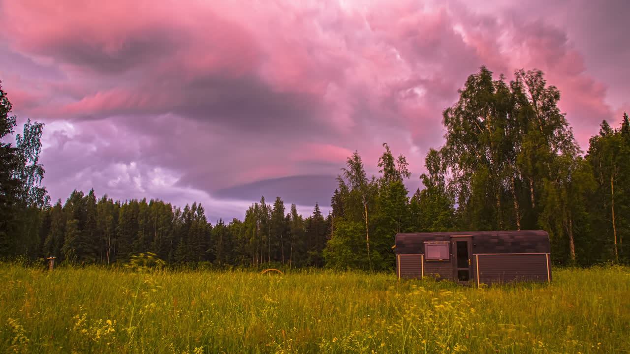 timelapse de nubes pesadas sobre un bosque boreal verde y un prado con una cabaña rural de madera termo