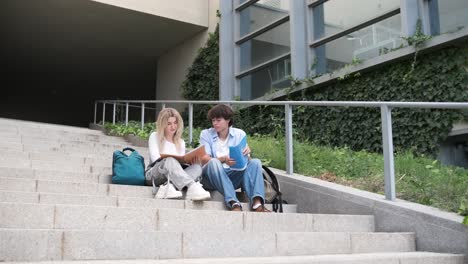 Young friends reading book on steps outside university building