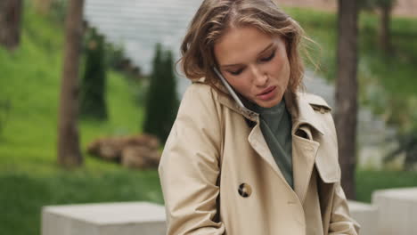 caucasian female student talking on the phone while writing in a notebook outdoors.