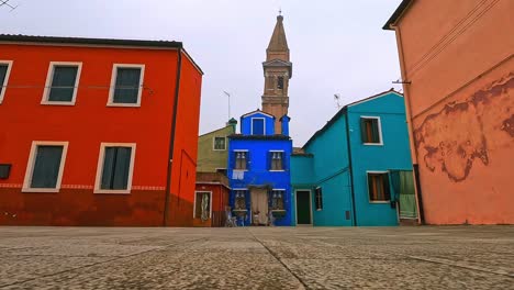 Low-angle-ground-surface-fpv-pov-toward-colorful-houses-and-leaning-belltower-of-Burano-in-Italy