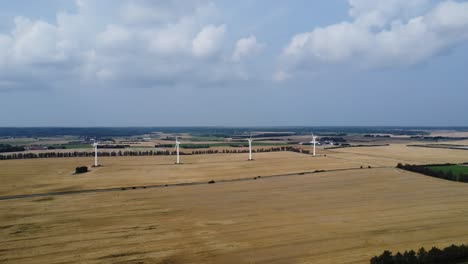 4-Turbinas-De-Viento-En-Un-Prado-Con-Hermosas-Nubes-En-El-Cielo-De-Fondo,-Droneshot