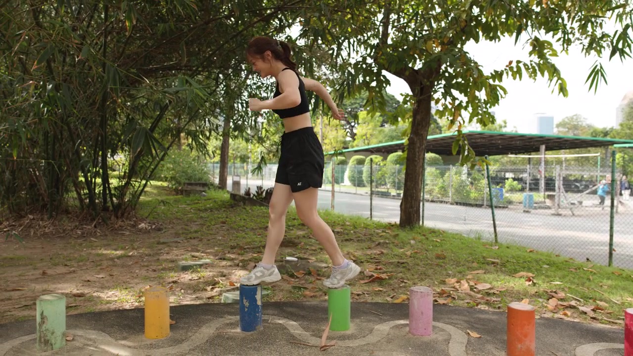 Una mujer tailandesa en forma realiza ejercicios de equilibrio en postes coloridos en un parque soleado al aire libre