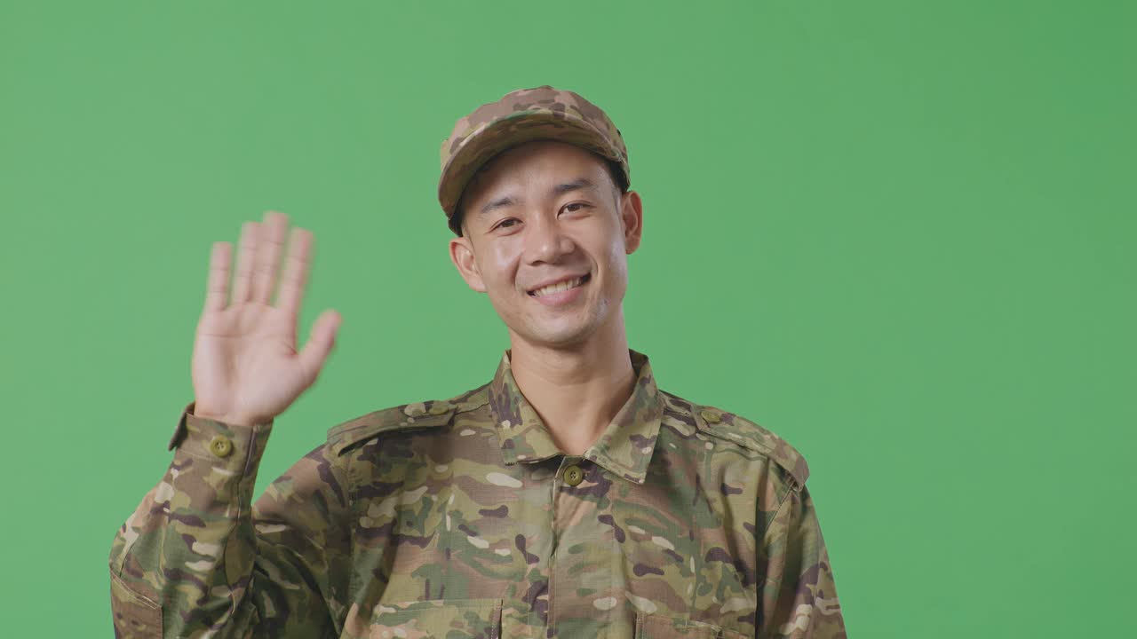 Close Up Of Asian Man Soldier Smiling, Waving Hand, And Saying Bye While Standing In The Green Screen Background Studio