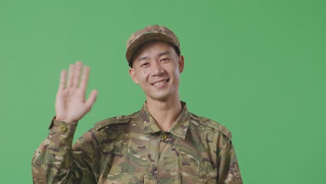 close up of asian man soldier smiling, waving hand, and saying bye while standing in the green screen background studio
