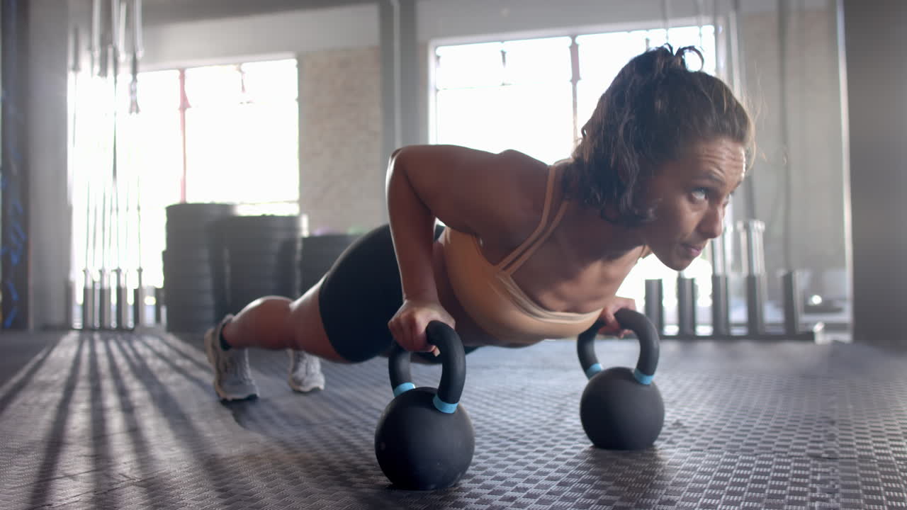 Doing push-ups using kettlebells, woman exercising in gym for fitness