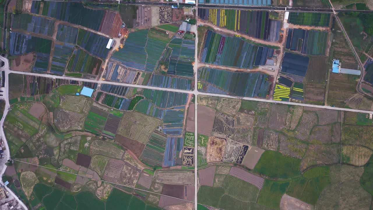 Top-down drone shot of colorful patchwork farmland in Huishui, Guizhou, showing fields, greenhouses, rural roads and agricultural patterns across a vibrant countryside landscape. China