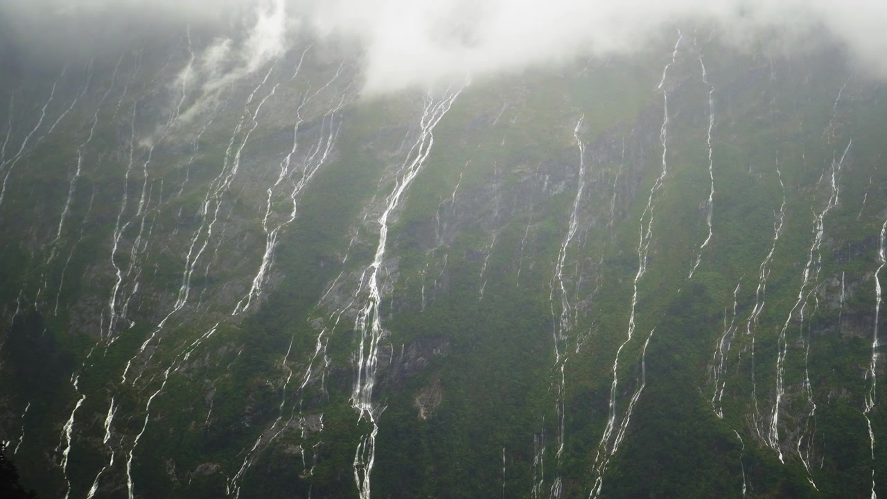 Lavvinkelbillede af flere vandfald i Milford Sound under kraftig regnvejr. Forhistorisk New Zealand