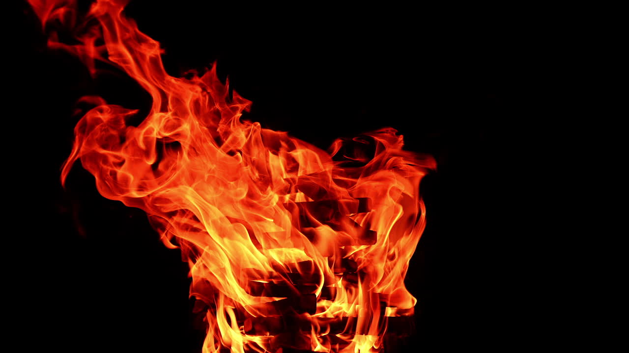 High stack of wooden logs burn in the bonfire. Dangerous tongues of red flames stretch into the air at night.