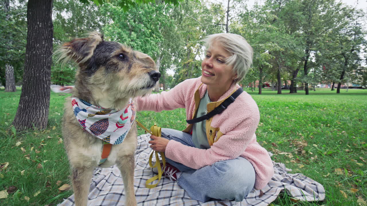 Smiling Woman Sitting on Blanket and Petting Her Dog in Park