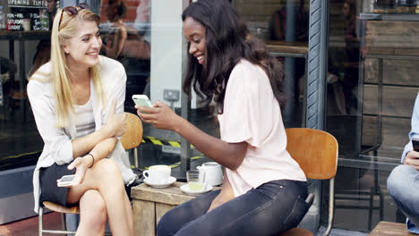 amigas compartiendo juntos usando un teléfono inteligente en un café urbano