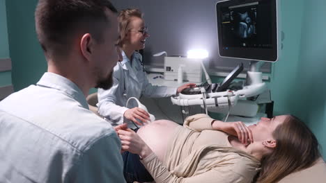 female gynecologist showing image of fetus on screen of ultrasound machine to happy future parents