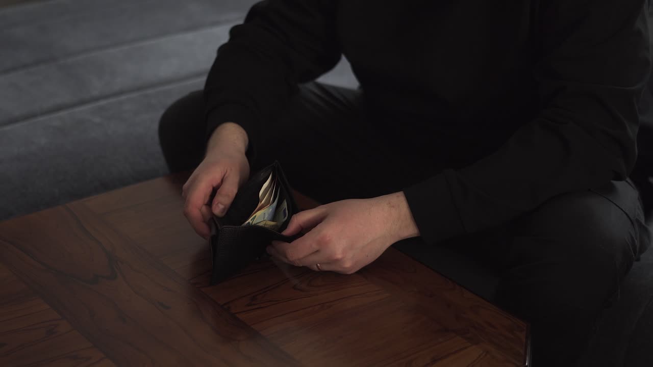 Man sitting on a couch counts cash in his wallet, useful for budget, finance, and payday concept footage