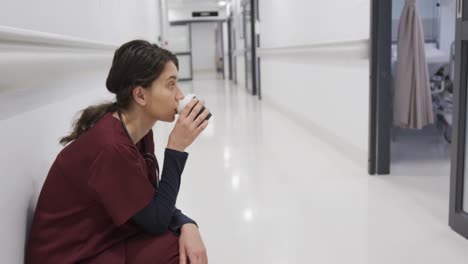 doctora caucásica en cuclillas y bebiendo café en el pasillo del hospital, cámara lenta