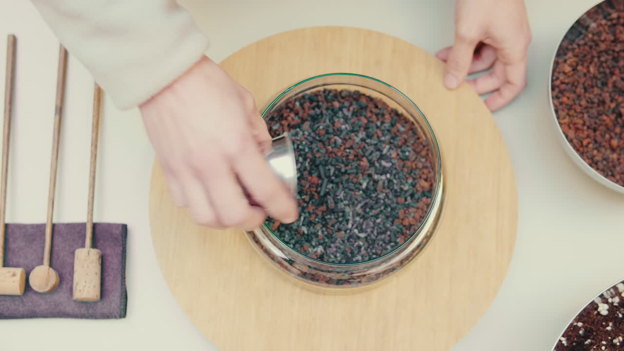 Manos vertiendo grava en un recipiente de terrario de cristal