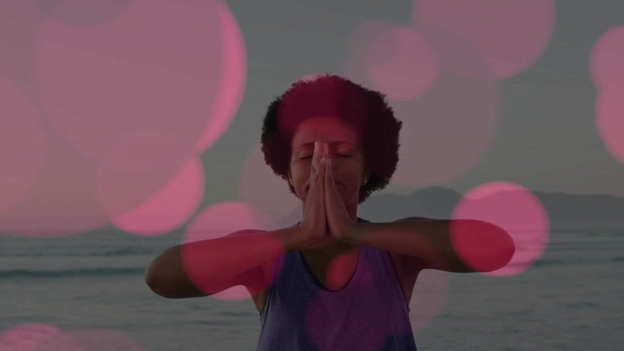 Woman at sea, palms starting up, lowering into prayer for health, pink bokeh growing over subject