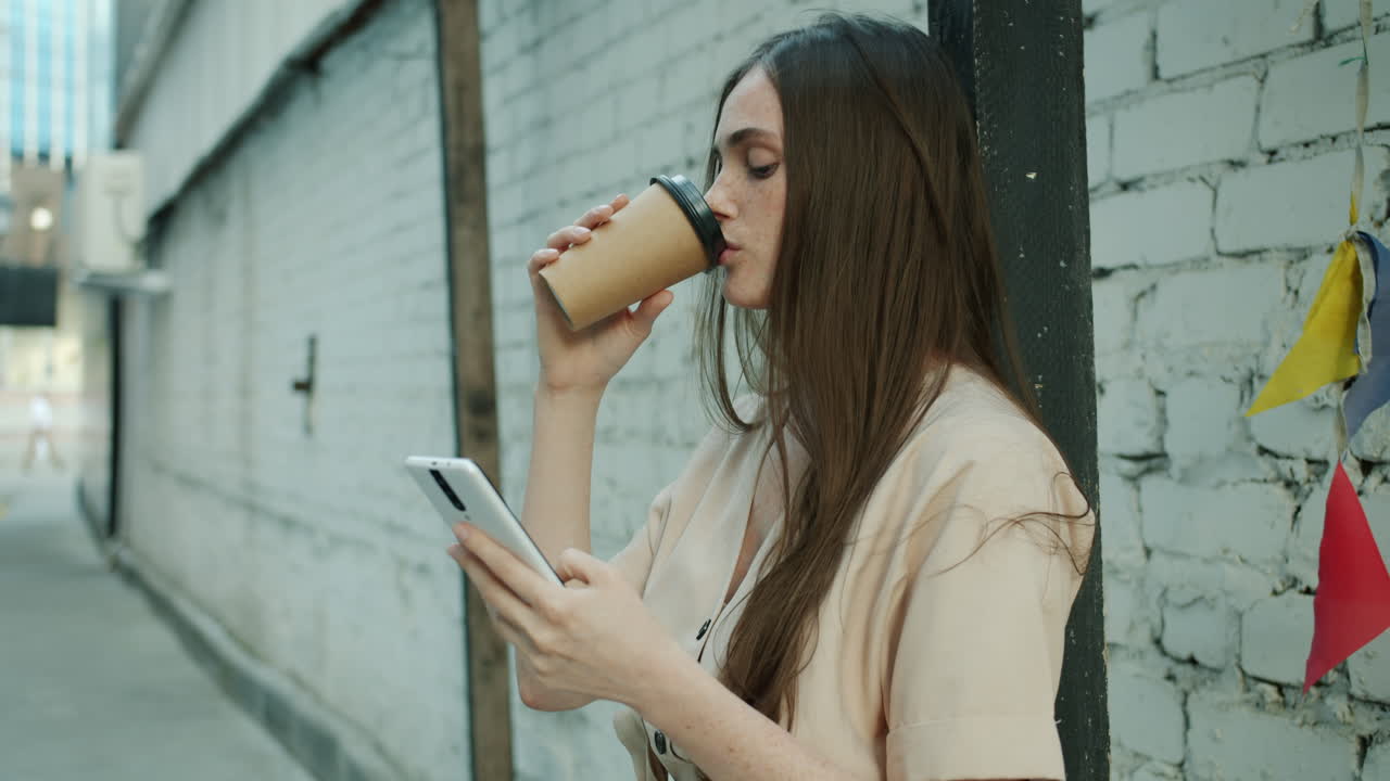 Woman drinking coffee and using a smartphone in a city alley