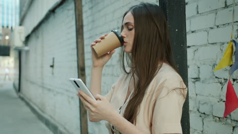 woman drinking coffee and using a smartphone in a city alley