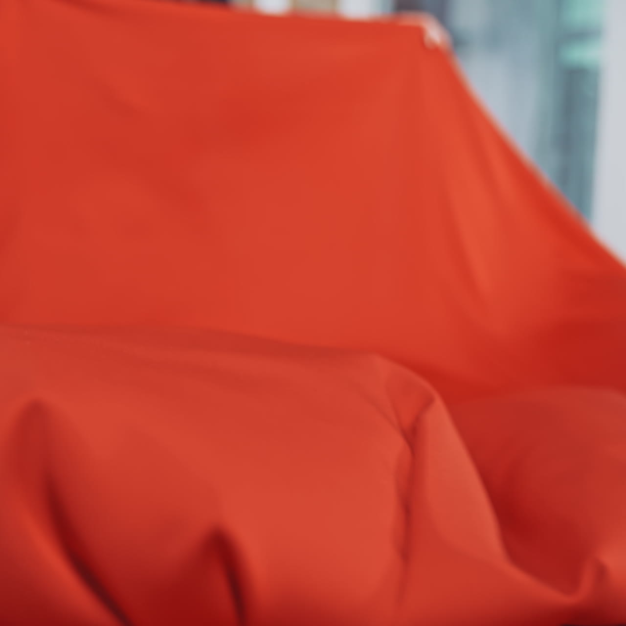 Young seamstress is putting bright red fabric on the wooden table. Large piece of red material in the hands of a dressmaker in workshop.