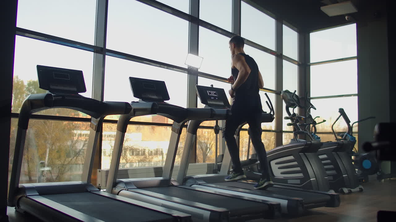Young athletic men and women exercising and running on treadmill in sport gym. Slow motion Near a large panoramic window