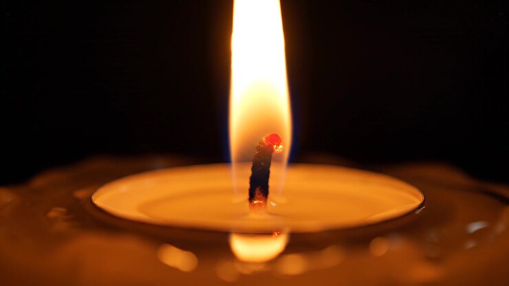Primo piano di una fiamma di candela che brucia su sfondo scuro.