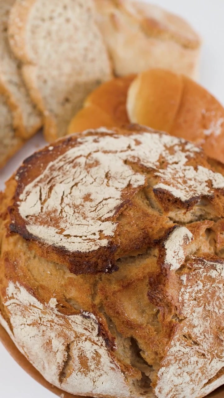 High angle slow rotation of crusty sourdough loaf with sliced baguette and pastries behind.