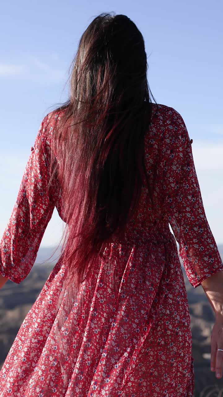 Woman in a red dress with long hair looking at a scenic mountain landscape