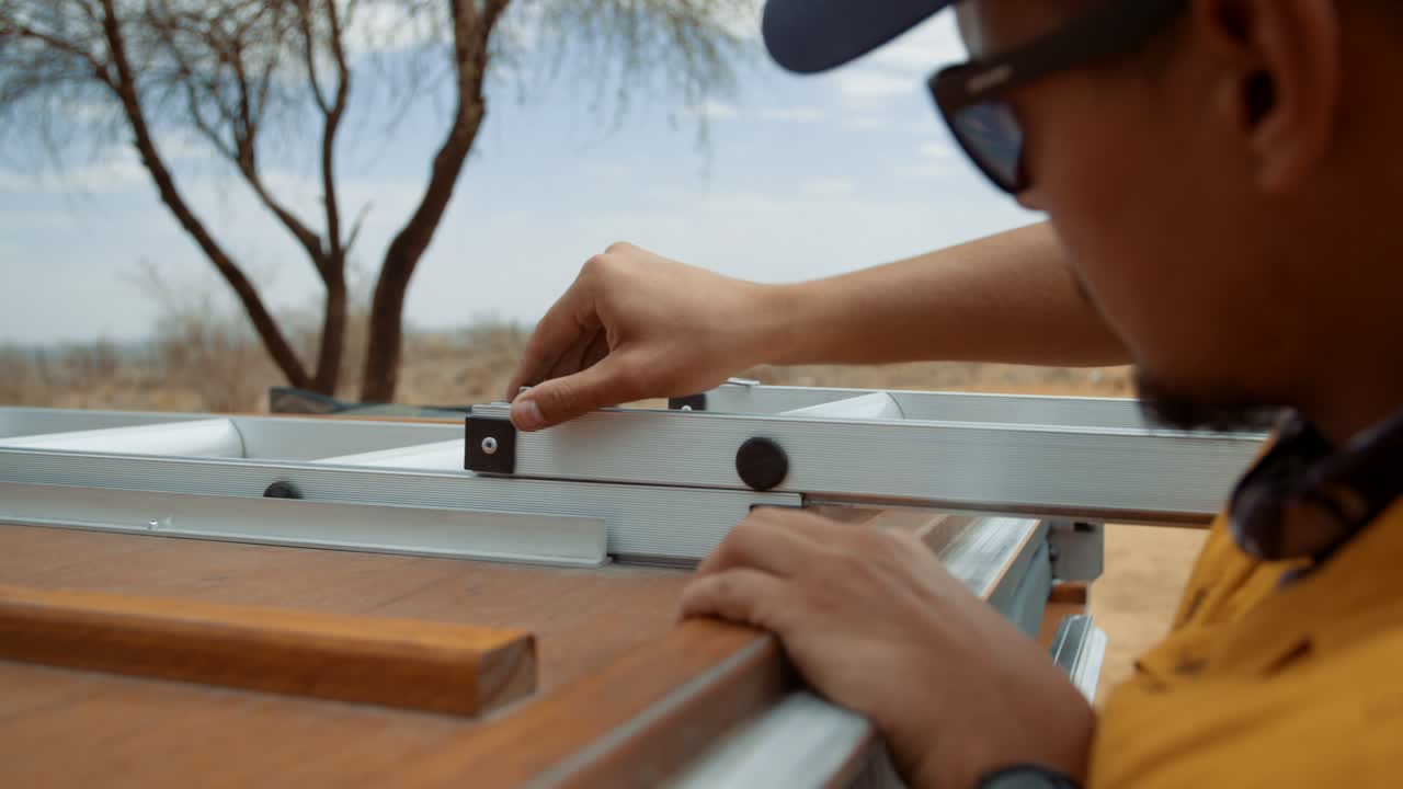 Static shot of a Caucasian male tourist in Africa as he pulls out the ladder of a rooftop tent and checks that the safety pins are in