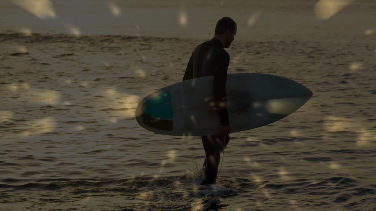Man carrying surfboard walking into golden water at sunset, displaying floating technology icons
