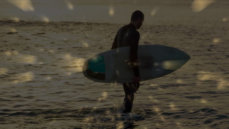 man carrying surfboard walking into golden water at sunset, displaying floating technology icons